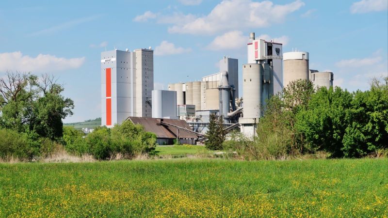 Das Bild zeigt eine Industrieanlage vor einer grünen Landschaft. 