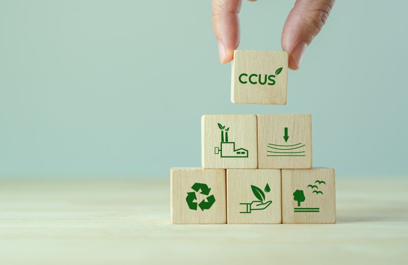 Holzwürfel mit Symbolen für Industrie, CO₂-Speicherung, Recycling und Umweltschutz, darüber ein Würfel mit der Aufschrift CCUS.
